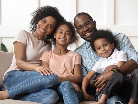 Portrait of happy young african American family with little kids sit relax on couch cuddling, smiling black parents rest on sofa hug preschooler children posing for picture at home together